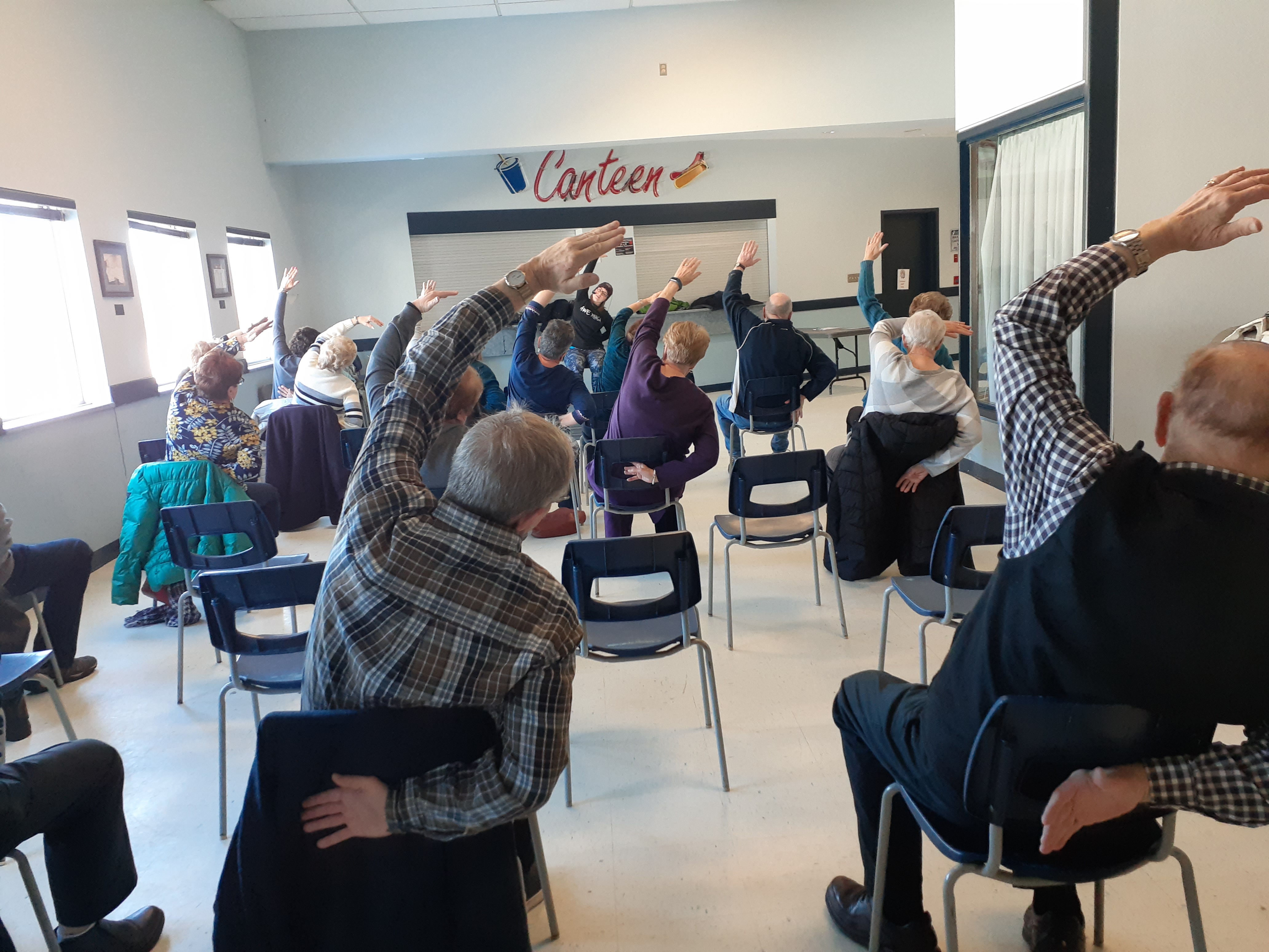 Participants sitting in chairs leaning to the side with one arm above head stretching