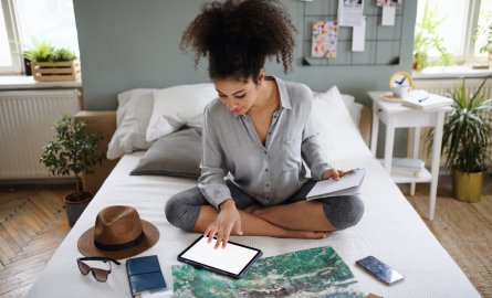 A woman sitting on a bed planning a trip.