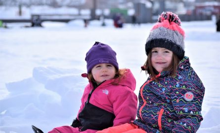 Two smiling children sitting outside in winter.