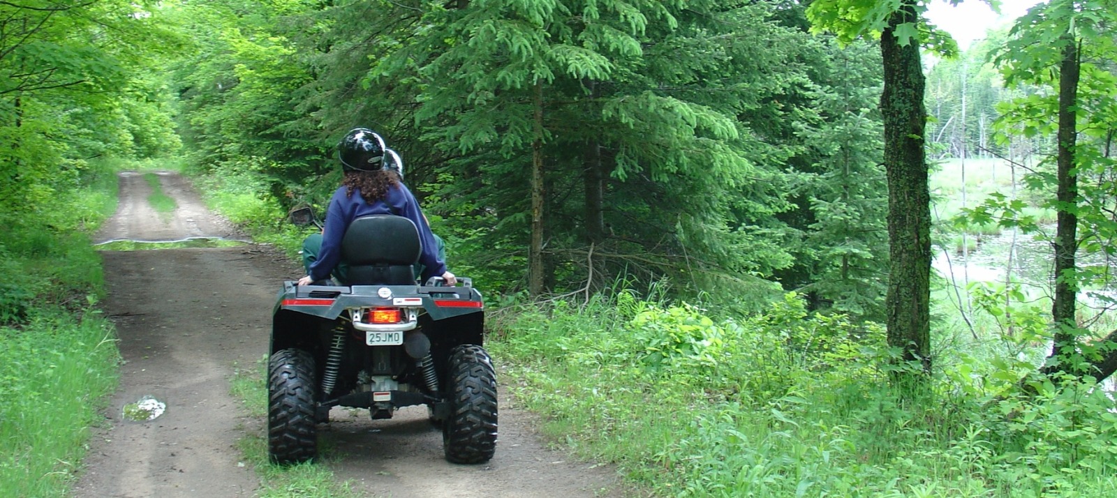 Two ATVs are driven through a forested trail.