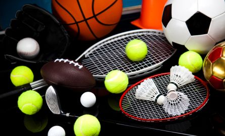 A pile of soccer balls, tennis balls, golf balls and tennis rackets.