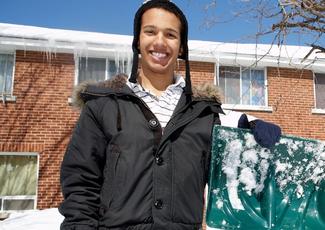 A young man holding a snow shovel outside a building.
