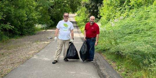 Two men with garbage bags on a walking path.