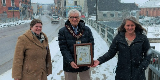 Three people on a sidewalk holding a certificate.