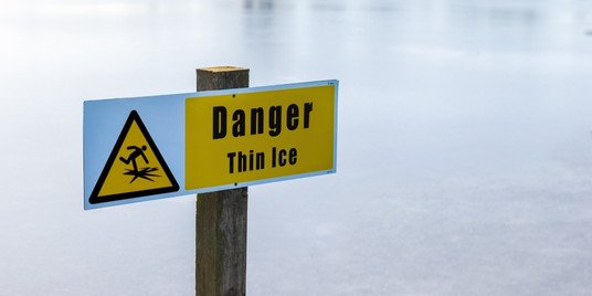 A sign that reads "Danger: Thin Ice" overlooking a frozen body of water.