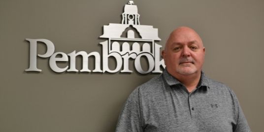Man stands in front of a sign that says Pembroke.