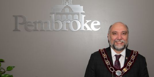 A man standing in front of a sign that says "Pembroke".