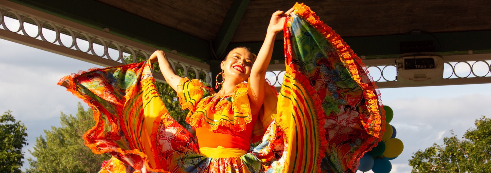 A woman smiling and dancing while wearing a colourful dress.