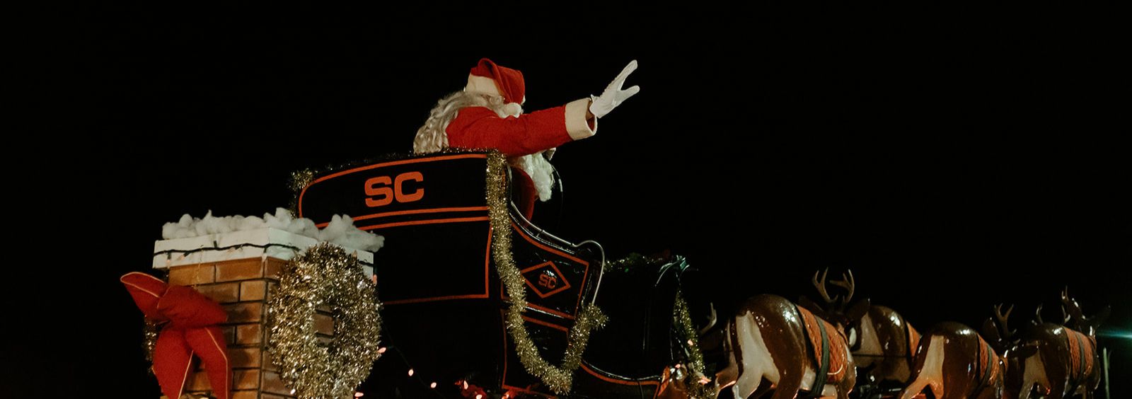 Santa Claus riding in a sleigh on a parade float waving at a crowd.