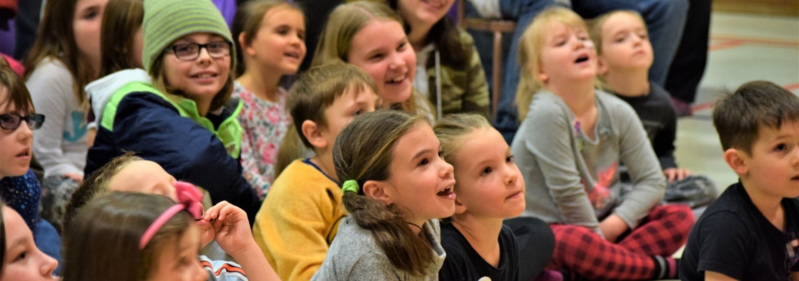 A group of kids sitting in a gymnasium.