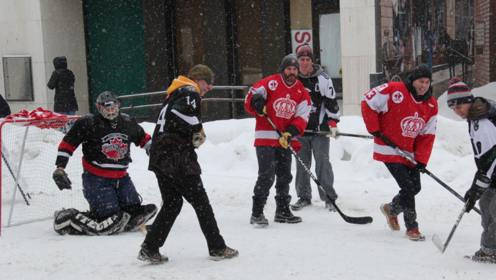A group of men playing road hockey in the winter.