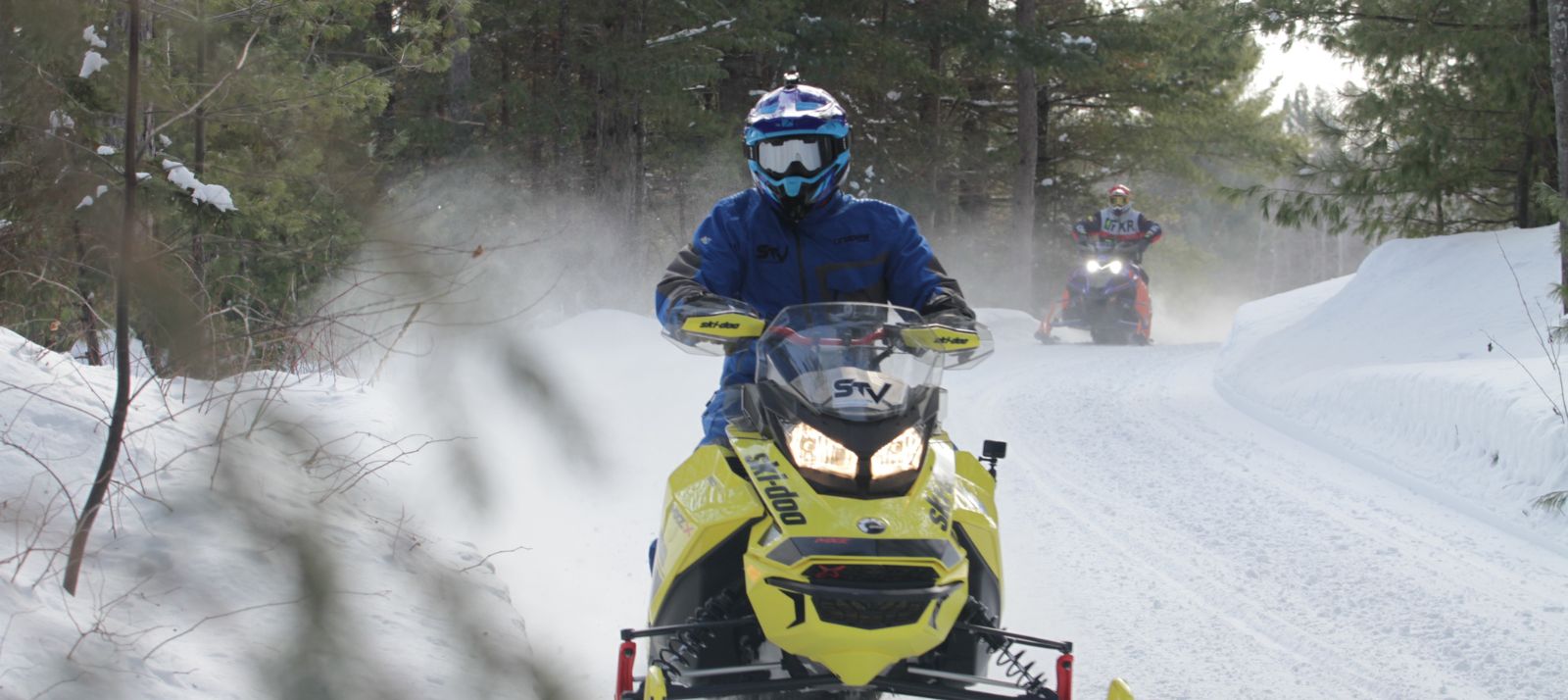 Two people snowmobiling on a trail.